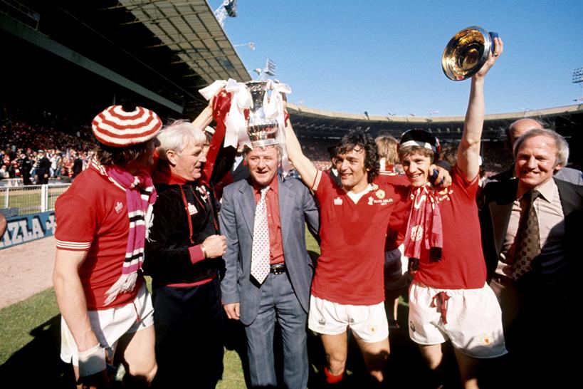 FA Cup Finale 1977 - Liverpool vs Manchester United - Wembley Stadium. Manchester United Manager Tommy Docherty (Mitte) feiert mit Lou Macari (dritter rechts) und Gordon Hill (zweiter rechts) den FA Cup. Fot: PA Images / Alamy Stock Foto